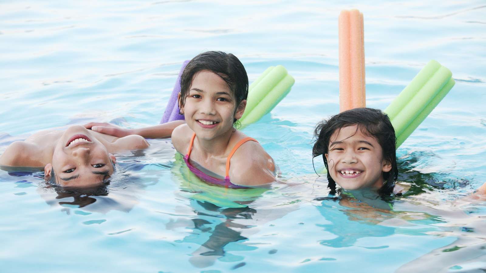 Three kids swimming in pool with noodles