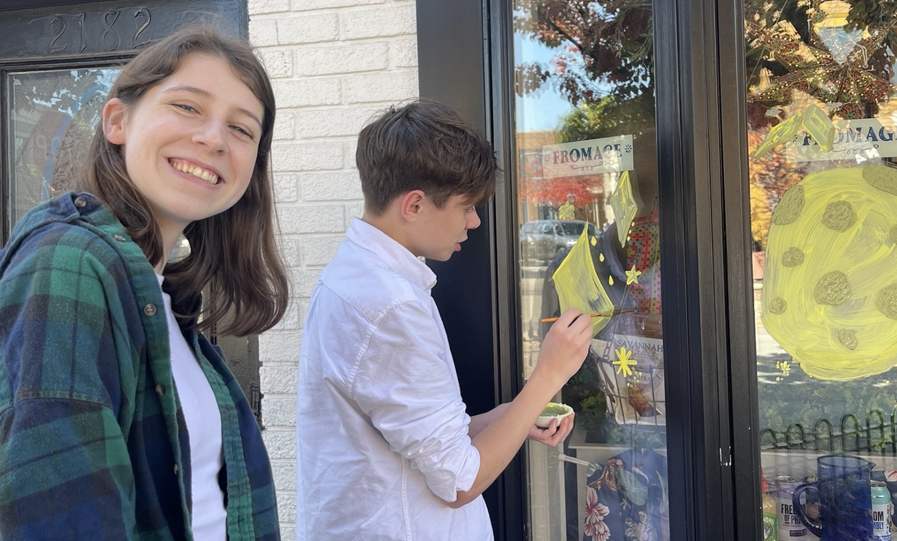 Two students paint a storefront window